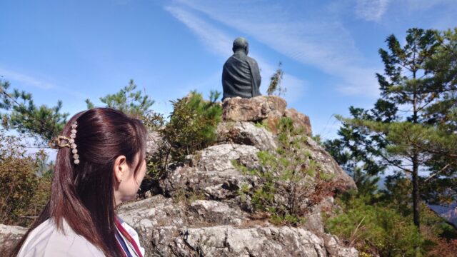 お遍路の格好をして、弘法大師の像の後ろにいる写真